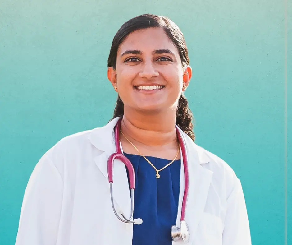 Dr. Coimbatore smiling in a white doctor coat and stethoscope in front of gradient teal background