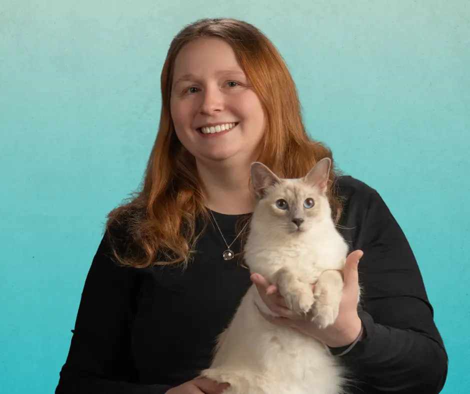 Ashley Dzubak, Managing Veterinarian of AcutePet Grove City smiling and holding a cat in front of a gradient teal background