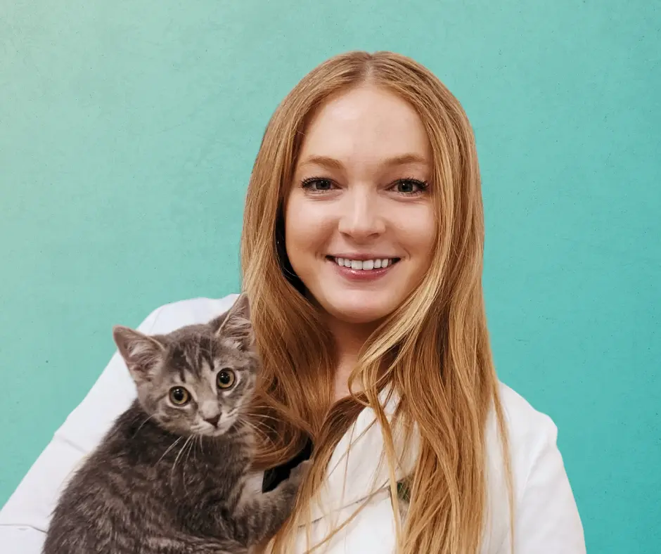 Dr. Meghan Barnes, Associate Veterinarian at AcutePet Urgent Care in Voorhees Township, NJ smiling holding a kitten in her arms on a gradient teal background